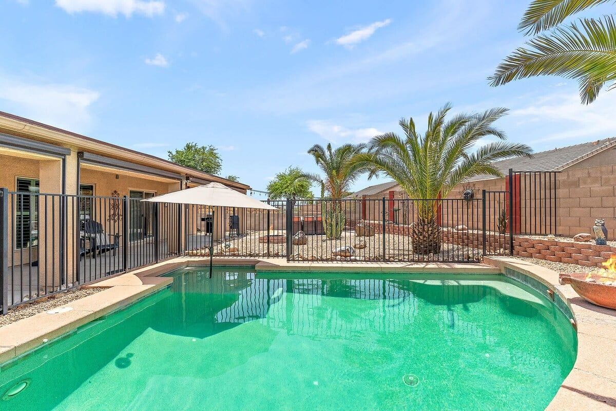 Une piscine entourée d’une clôture, un patio couvert et des palmiers.