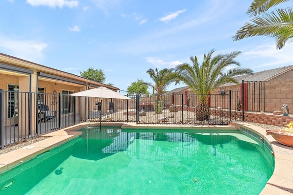 Una piscina con zona vallada, un porche cubierto y palmeras.