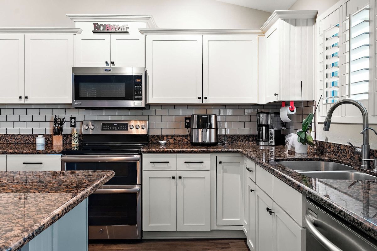 A modern kitchen with white cabinets, a stainless steel microwave, a built-in oven, and a granite countertop.