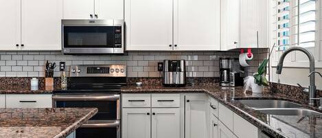 A modern kitchen with white cabinets, a stainless steel microwave, a built-in oven, and a granite countertop.