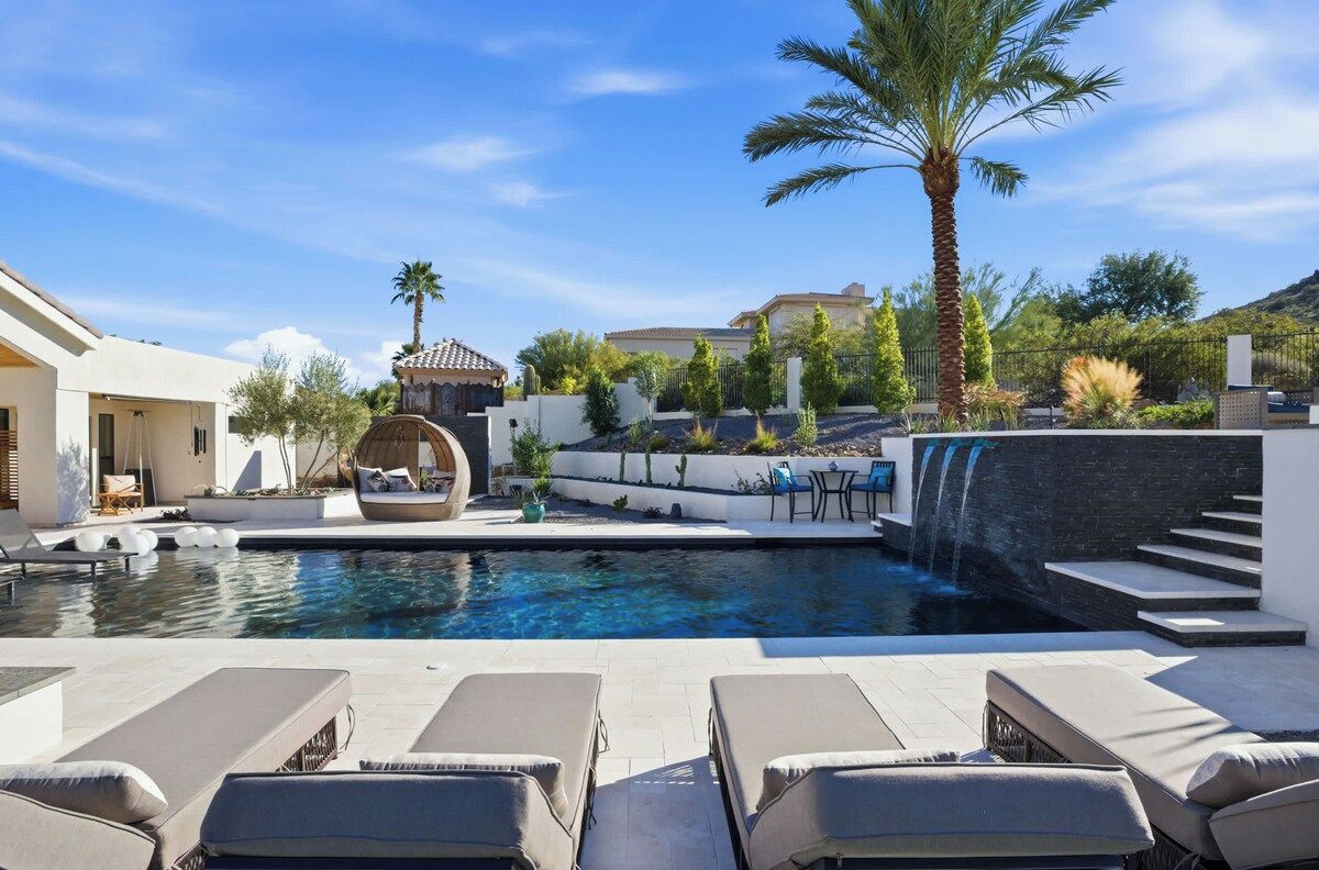A swimming pool with lounge chairs, a palm tree, and a waterfall feature.