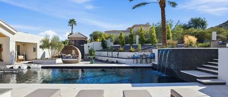 A swimming pool with lounge chairs, a palm tree, and a waterfall feature.
