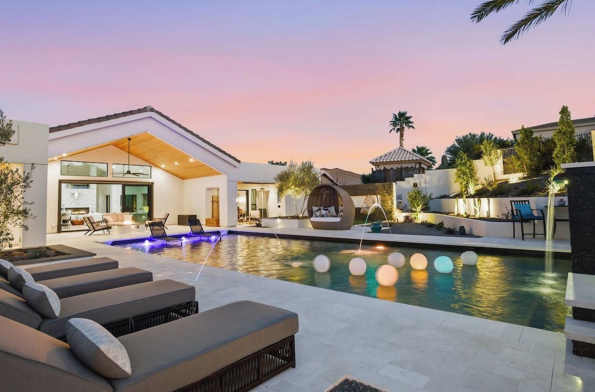 Een modern buitenzwembad met ligbedden, een jacuzzi en een goed verlicht terras.