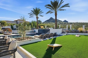 A pool area with artificial grass, lounge chairs, and palm trees. - Dos Palms | Luxury | HtdPool, Jacuzzi, Trails! (Phoenix)