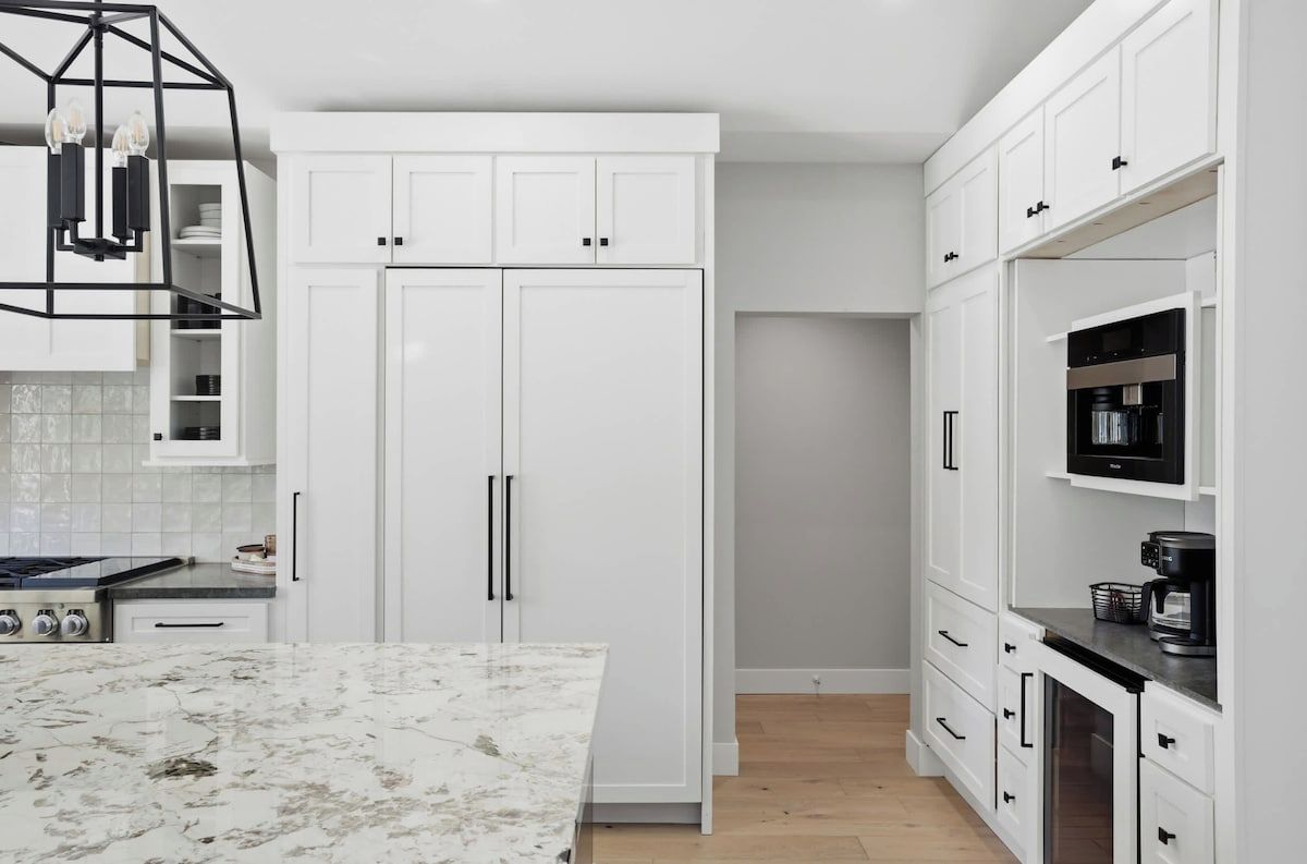 A kitchen with white cabinetry, a marble countertop, and a built-in stove.