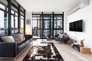 A modern living room with a large window, a flat-screen TV, and a leather sofa. - Scenic Penthouse Living in the Heart of Melbourne (Southbank)