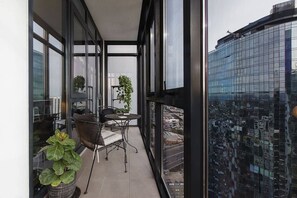 Un balcon avec une table et des chaises, de grandes fenêtres et une vue sur le paysage urbain.