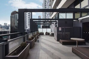 Eine Dachterrasse mit modernem Design, ausgestattet mit einer Sitzecke, Tischen, Stühlen, Pflanzen und Blick auf die Stadtlandschaft.
