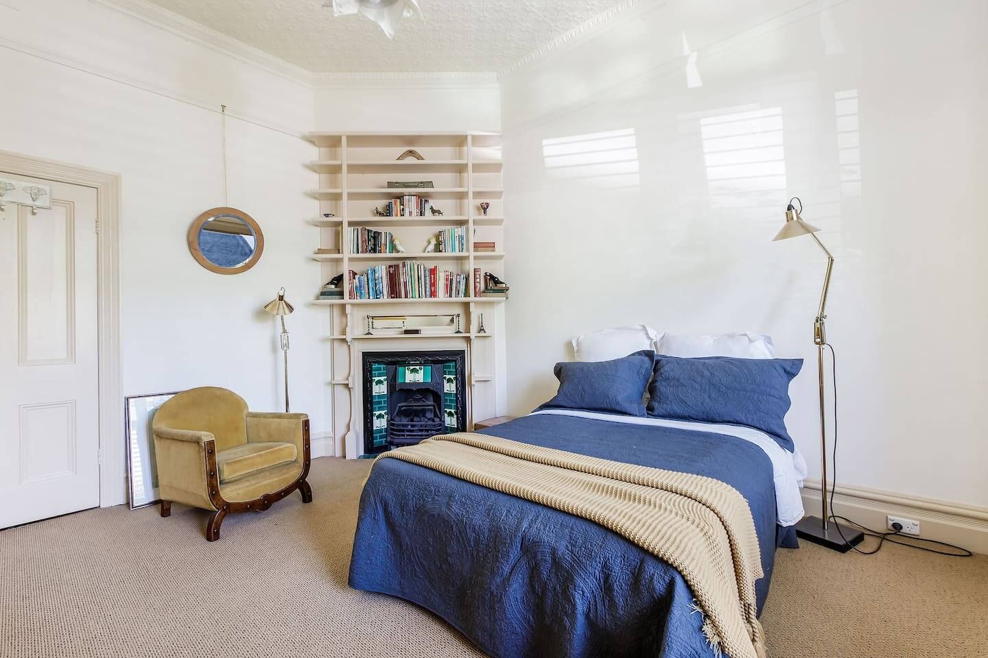 A bedroom with a bed, a chair, a bookshelf, and a fireplace.