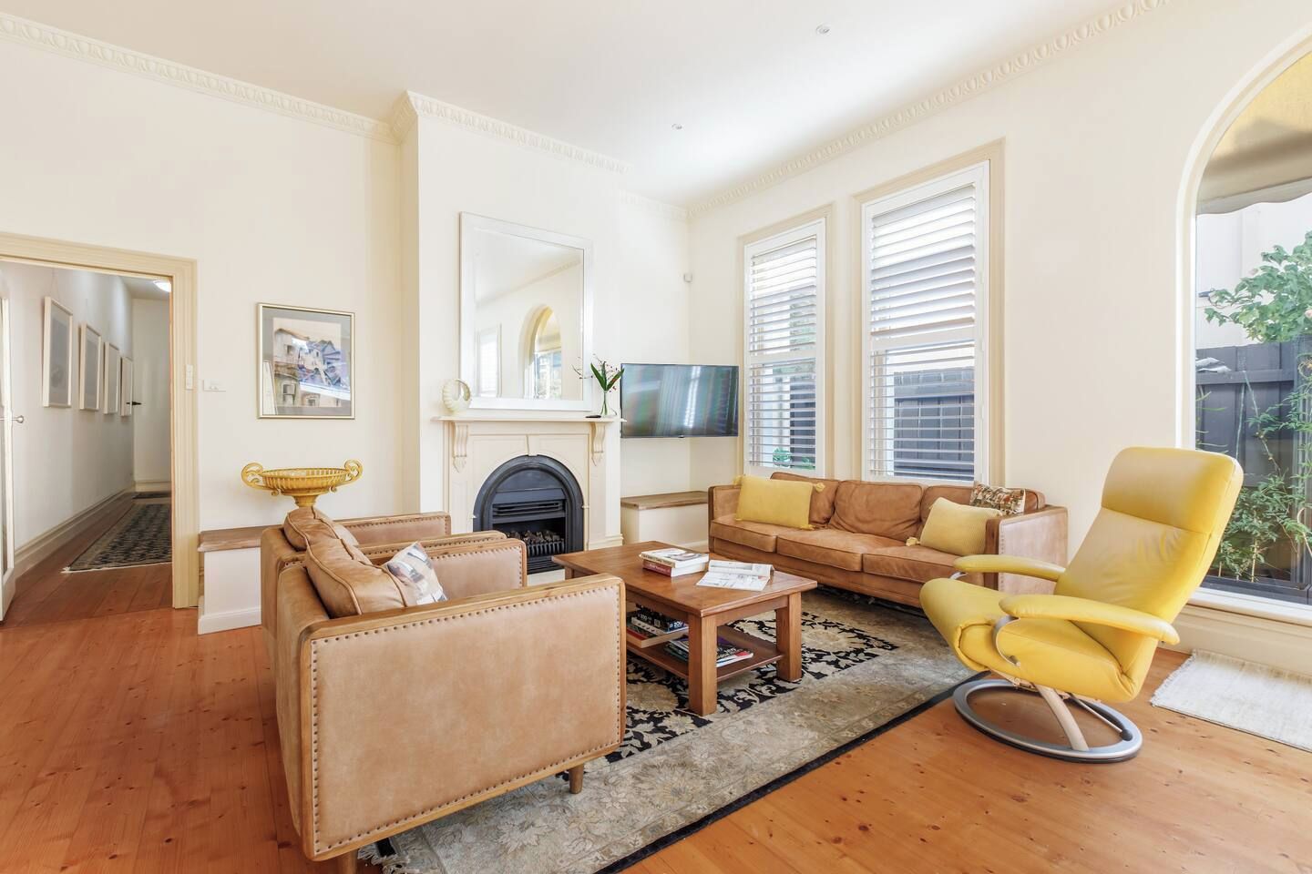 Een woonkamer met een open haard, een zithoek, een gele fauteuil en een televisie.