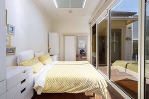 Ein Schlafzimmer mit Bett, Kleiderschrank, Schreibtisch und einer Glastür, die zu einem Außenbereich führt.