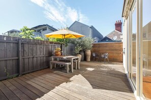 Eine Holzterrasse mit Tisch und Stühlen, einem gelben Sonnenschirm und Topfpflanzen.