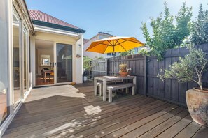 Een houten terras met een tafel, stoelen, een plant in pot en een gele parasol.