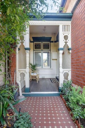 A covered porch with a tiled floor, a window with shutters, and a number 29 sign on a column. - The Sussex Vintage Haven near Albert Park Lake (South Melbourne)