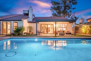 Ein modernes Haus mit Schwimmbad, überdachter Terrasse und gepflegtem Rasen.
