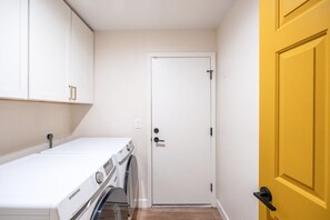 Uma lavanderia com máquina de lavar, secadora e uma porta branca.
