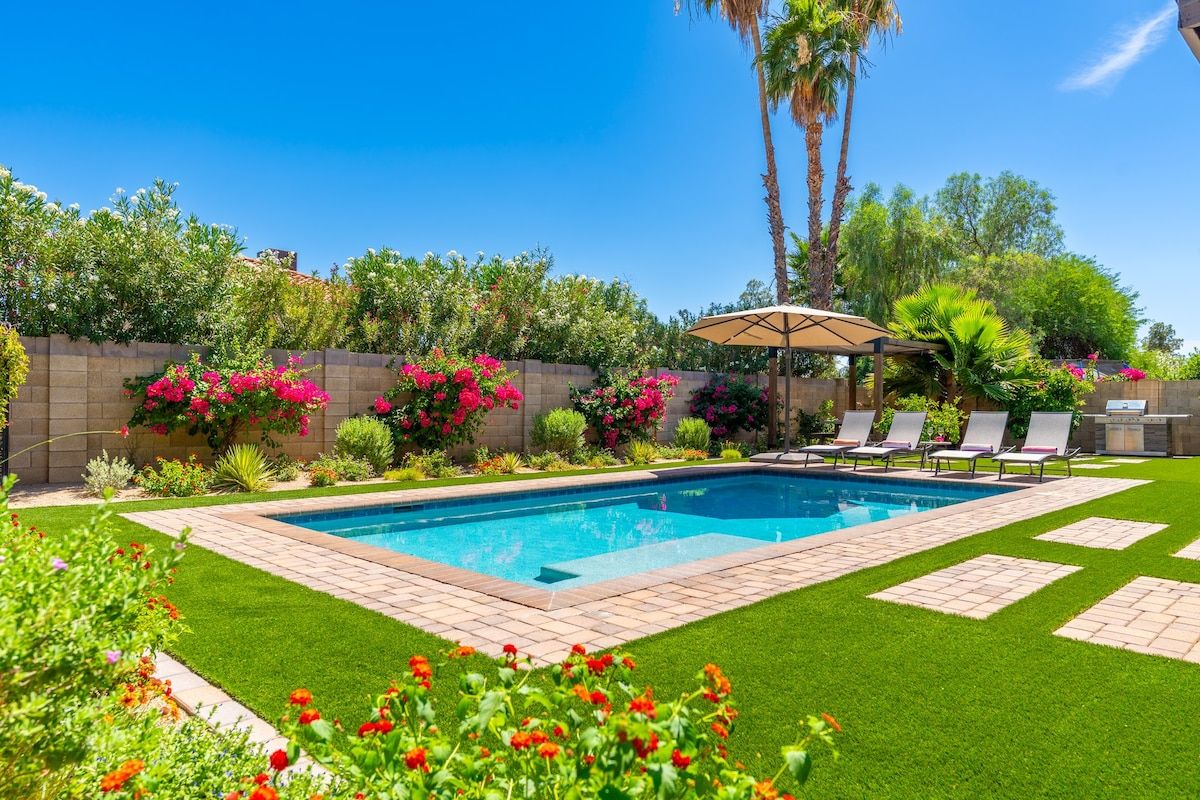 A swimming pool with a tiled deck, surrounded by a well-maintained lawn and various plants.