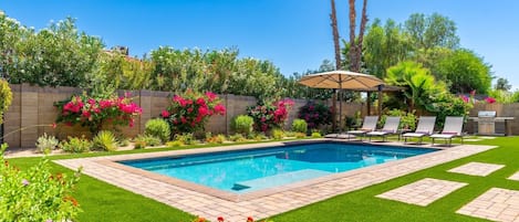 A swimming pool with a tiled deck, surrounded by a well-maintained lawn and various plants.