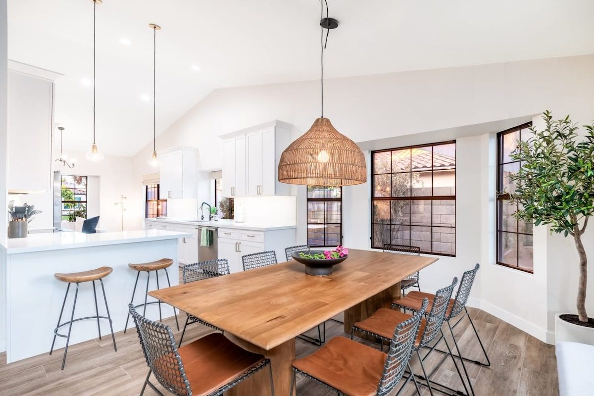 A modern kitchen with a wooden dining table, bar stools, and pendant lighting.
