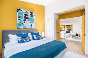 Ein modernes Schlafzimmer mit einem großen Bett, einem Bild an der Wand und einem offenen Durchgang zu einem Wohnbereich.