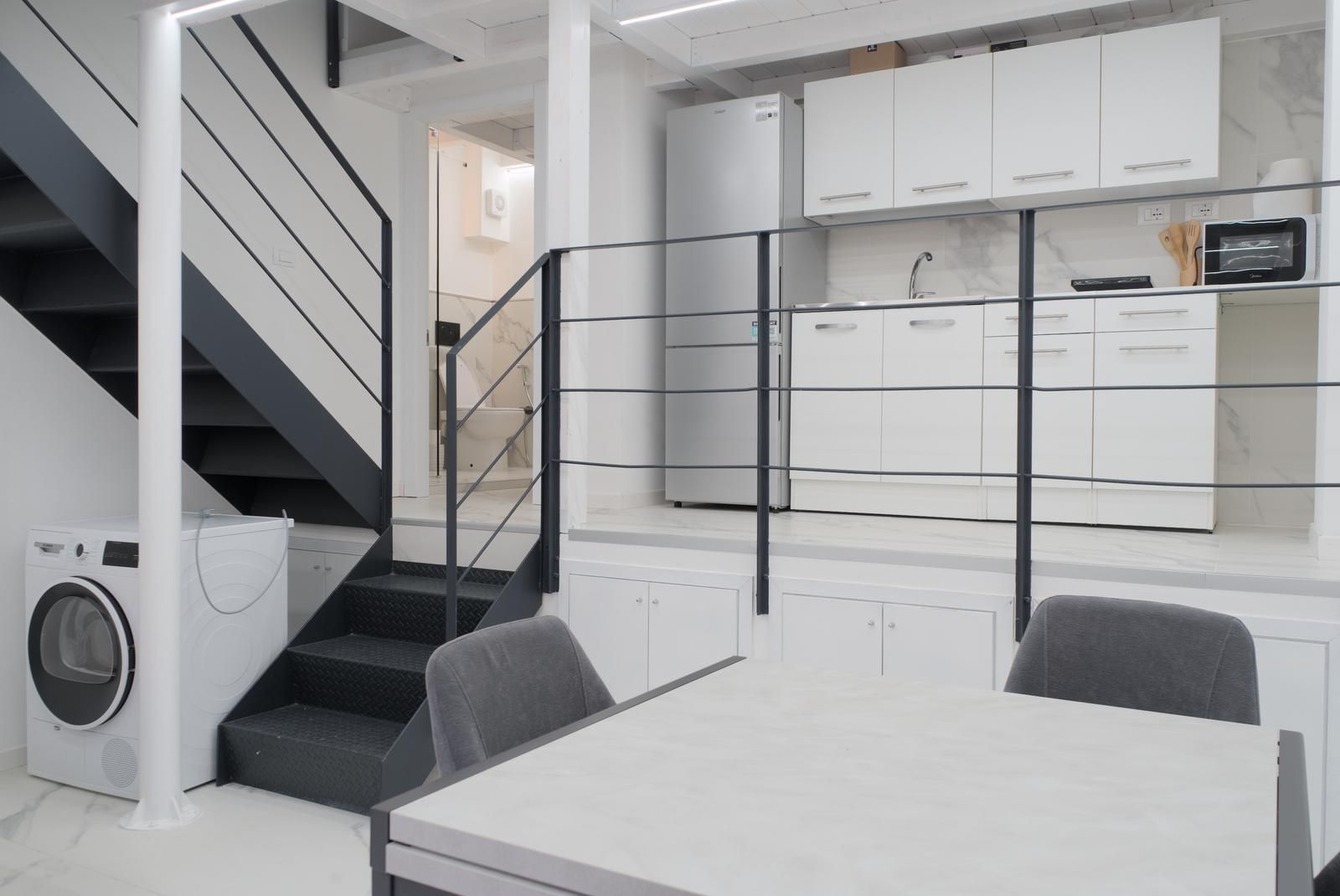 A modern kitchen with white cabinets, a built-in oven, and a dining area with a table and chairs.