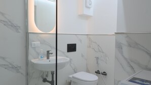 Un baño con mampara de vidrio, lavamanos, inodoro y ducha.