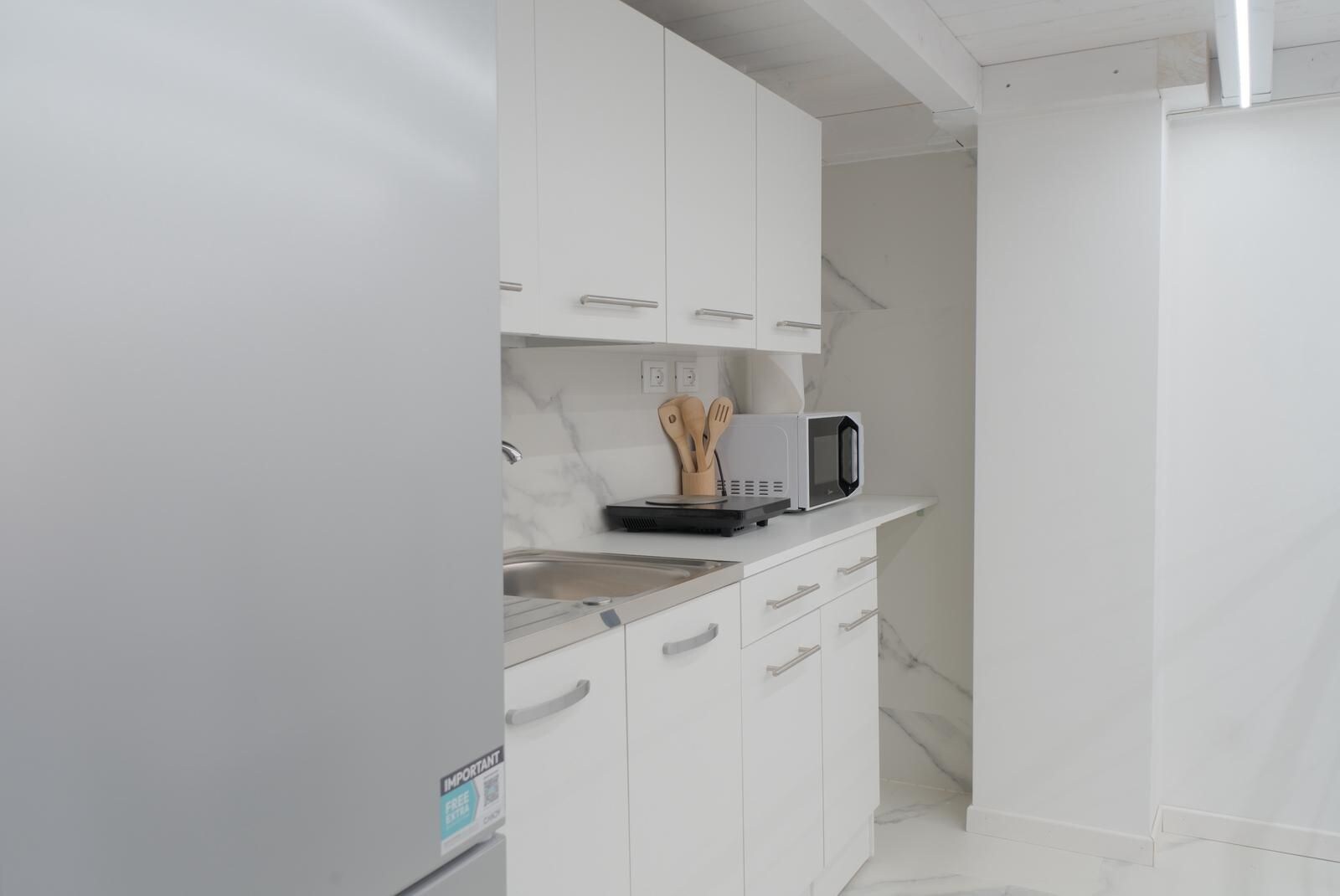 Une cuisine moderne avec des meubles blancs, un évier en acier inoxydable et un four à micro-ondes posé sur le plan de travail.
