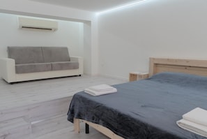Quarto com cama, sofá, mesa de cabeceira e ar condicionado.