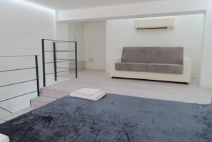 A modern living room with a sofa, a black rug, and a staircase with a metal railing. - Appartmento Gavi • Elegante e Centrale (Verona)