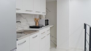 Una cocina moderna con armarios blancos, un lavamanos de acero inoxidable y un microondas.