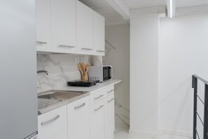 Cozinha moderna com armários brancos, pia de aço inoxidável e micro-ondas.