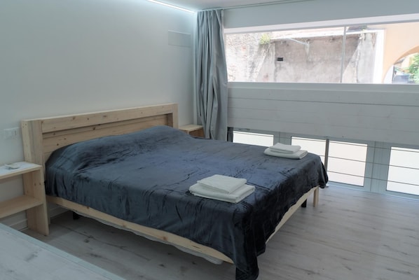 Quarto com cama de madeira, mesa de cabeceira e janela com vista para o exterior.