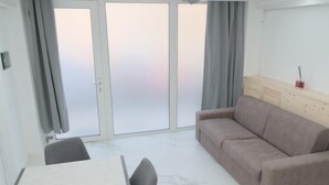 Una habitación moderna con sofá, una mesa de comedor y un ventanal corredero que da a un espacio exterior.