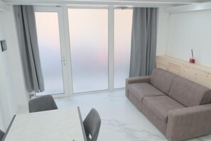 Quarto moderno com sofá, mesa de jantar e porta de vidro deslizante para área externa.