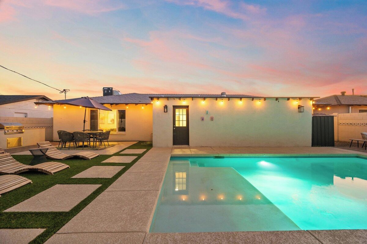 A backyard with a swimming pool, a barbecue area, and a patio with chairs.