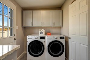 Une buanderie équipée de deux machines à laver à chargement frontal, avec un meuble de rangement au-dessus et une fenêtre sur le côté gauche.