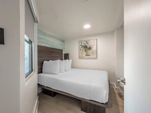 A single-bed room with a wooden headboard, a window, a painting on the wall, and a door with a handle. - Stunning Oceanfront 1 Bedroom Condo Yachtsman 1006 (Myrtle Beach)