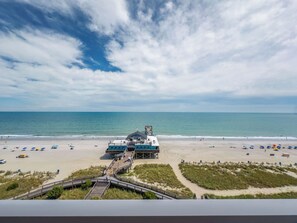 A beachside building with a deck overlooking the ocean, a sandy beach with umbrellas, and a boardwalk leading to the beach. - Stunning Oceanfront 1 Bedroom Condo Yachtsman 1006 (Myrtle Beach)