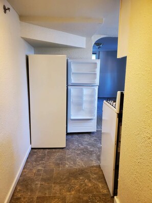 Ein schmaler Flur mit einem weißen Kühlschrank und einer weißen Gefriertruhe. Der Boden ist mit Fliesen ausgelegt, und die Wände sind in einer hellen Farbe gestrichen.