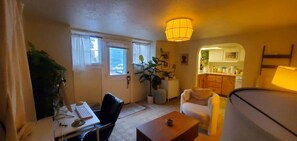 A living room with a desk, a chair, a sofa, a coffee table, and a kitchen area visible through an archway. - Fully Furnished 1-Bed Apartment in Cliff Cannon (Spokane)