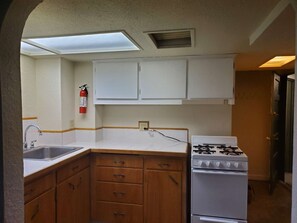 A compact kitchen with a gas stove, a sink, wooden cabinets, and a fire extinguisher. - Fully Furnished 1-Bed Apartment in Cliff Cannon (Spokane)