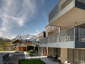 A modern multi-story building with balconies, a patio area with seating, and a view of mountains in the background. - Apartment in Rohrmoos-untertal With Balcony (Schladming)