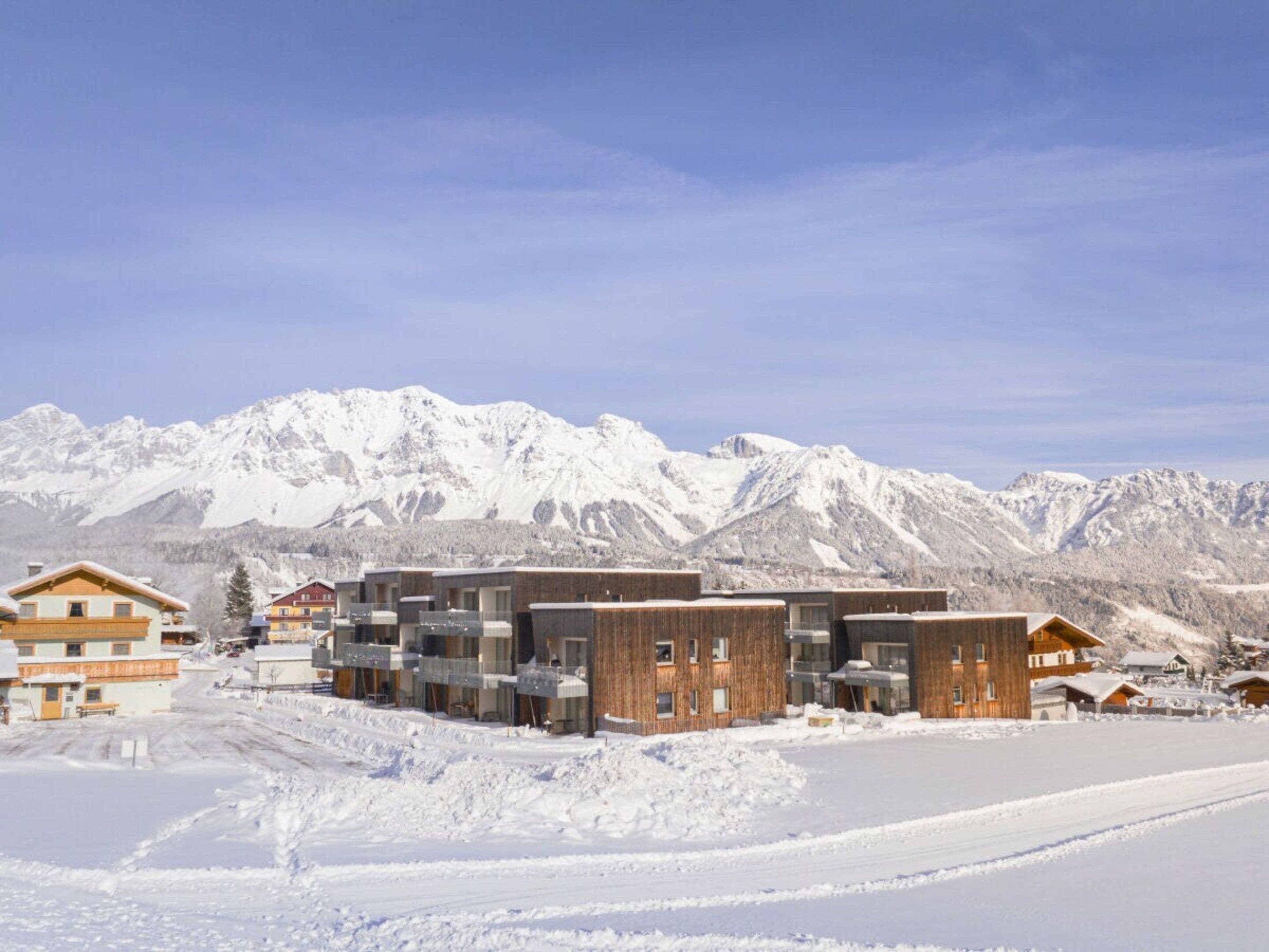 A snow-covered mountain resort with modern buildings, a clear sky, and a ski slope.