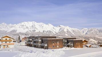 A snow-covered mountain resort with modern buildings, a clear sky, and a ski slope.