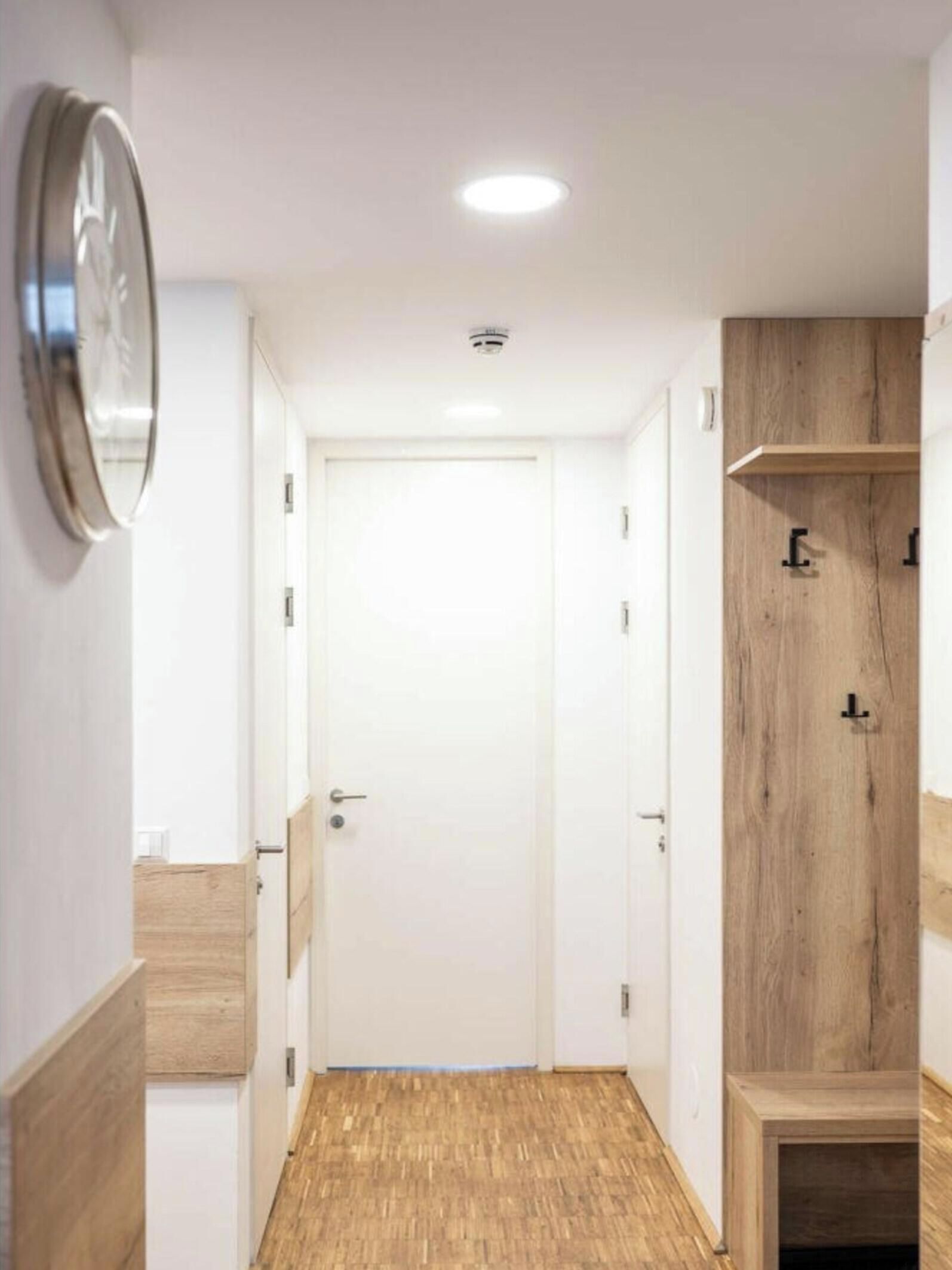 A hallway with a wooden floor, a white door, and a wooden cabinet with a mirror.