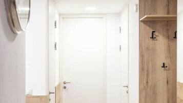 A hallway with a wooden floor, a white door, and a wooden cabinet with a mirror.