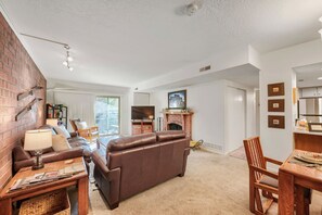 Ein Wohnzimmer mit Kamin, Ledersofas, einem Esstisch und einer Ziegelwand.