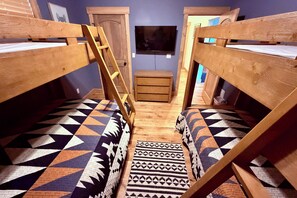 Ein Zimmer mit Etagenbetten, einer Hockerleiter, einem kleinen Holzschrank und einem gemusterten Teppich.
