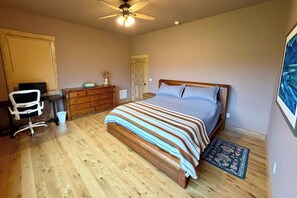 A bedroom with a wooden bed, a desk, a chair, a dresser, and a ceiling fan. - The Oar Lock Cottage (Ennis)