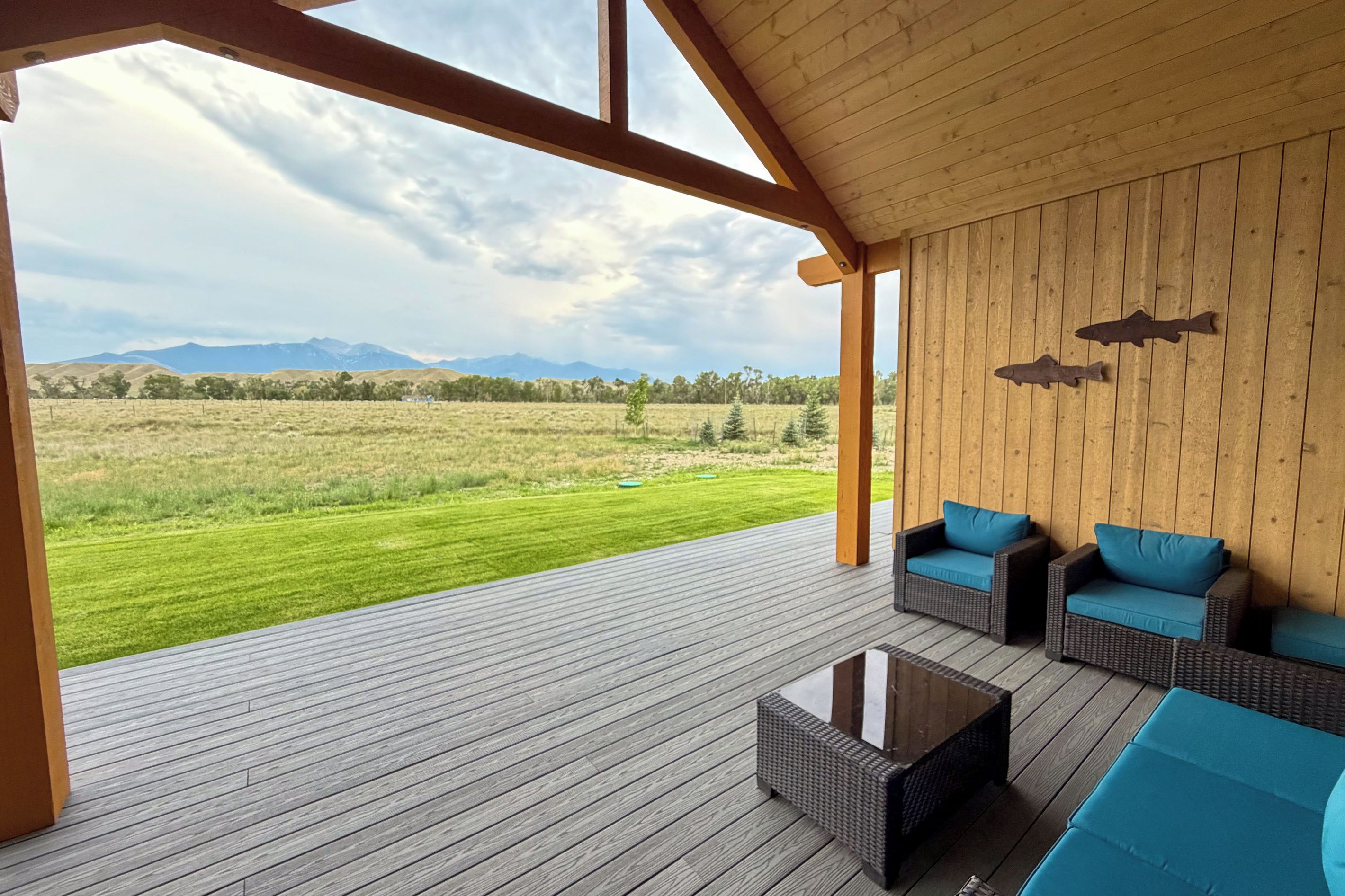 An outdoor deck with a view of a grassy field and mountains, furnished with wicker sofas and a coffee table.